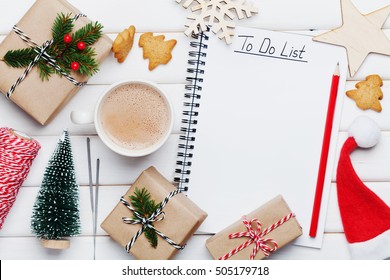 Cup Of Hot Cocoa, Holiday Decorations, Gift, Present, Miniature Fir Tree And Notebook With To Do List On White Wooden Table From Above. Christmas Or Winter Planning Concept. Flat Lay Style.