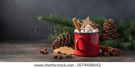 Cup of hot cocoa with marshmallow and cinnamon stick surrounded by spruce branches. Cozy seasonal holidays. Side view, dark background
