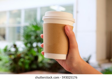 A Cup Of Hot Coffee With A Brown Paper Sleeve In Hand