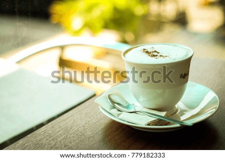 Cup of hot coffee (cappuccino or latte) decorated with powder coffee & milk forth on the surface serve on plate with tea, spoon and tissue, for beverage  background - healthy diet concept.