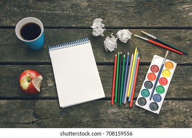 Cup hot coffee  notepad and blank sheet paper  colored pencils  paint  brushes   crumpled sheets paper the old wooden background  Workplace the artist  Never give up 
