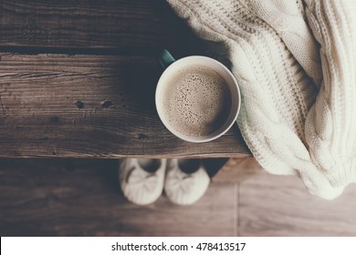 Cup Of Hot Coffee On Rustic Wooden Bench, Closeup Photo Of Warm Sweater With Mug And Slippers, Winter Morning Concept, Top View