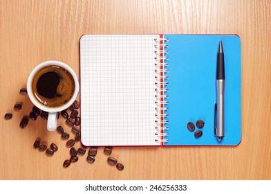 Cup of hot coffee, opened notebook and pen on wooden table, top view