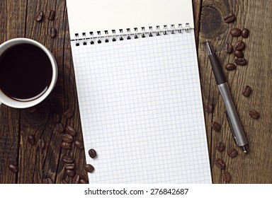 Cup of hot coffee, opened notebook and pen on wooden table, top view