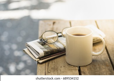 Cup of hot coffee, reading glasses and newspaper on wooden table in the garden morning - Powered by Shutterstock