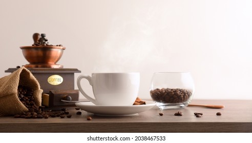 Cup Of Hot Coffee With Sack Full Of Beans And Manual Grinder On Wooden Table And White Isolated Background. Front View. Horizontal Composition.