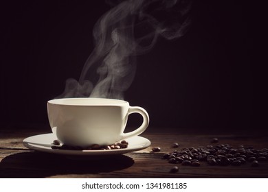 A Cup Of Hot Coffee With Steaming And Beans On Wooden And  Black Background. Hot Drink . With Steam,warm Soft Light, Dark Background.Good Morning Coffee And Have A Happy Day 