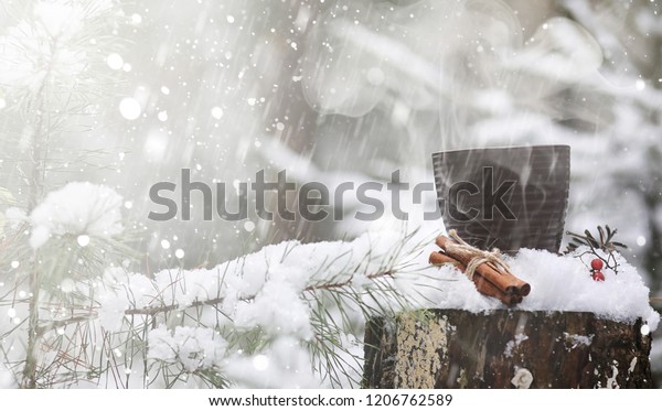A cup with a hot drink in the winter forest.\
Hot cocoa with cinnamon on the background of winter forest. First\
snow and hot chocolate.\
