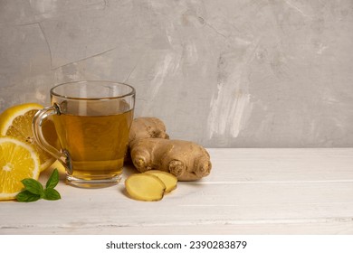 Cup of hot ginger tea with ginger root and lemon on gray background.