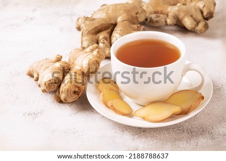 Cup of hot ginger tea with ginger root and slices  on gray background.