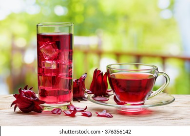 Cup Of Hot Hibiscus Tea (karkade, Red Sorrel, Agua De Flor De Jamaica) And The Same Cold Drink With Ice Cubes In Glass On Table At Terrace. Drink Made From Magenta Calyces (sepals) Of Roselle Flowers.