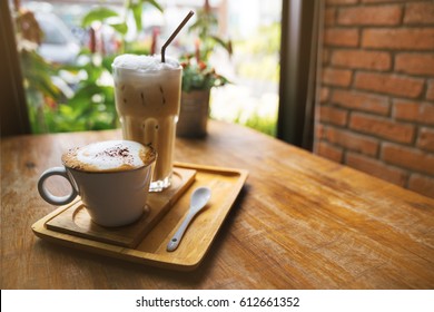 A Cup Of Hot Latte Coffee And Cold Coffee On A Wooden Table. A Stylish Modern Cafe With Wooden Tables And A Brick Wall.