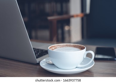 Cup Of Hot Latte Coffee And Laptop Computer On Wooden Table In Coffee Shop Co-working Space, Toned Image. Online Business, Working From Cafe, Portable Office Concept, Close Up