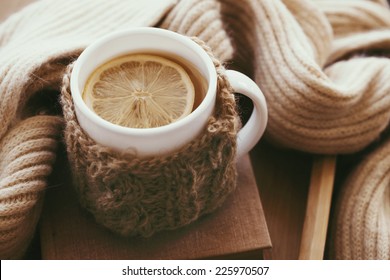 Cup of hot tea with lemon dressed in knitted warm winter scarf on brown wooden tabletop, soft focus