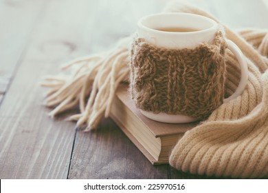 Cup of hot tea with lemon dressed in knitted warm winter scarf on brown wooden tabletop, soft focus
