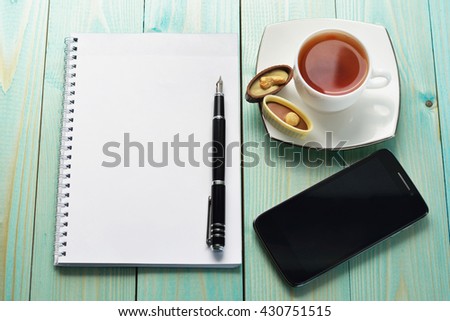 Cup Of Hot Tia Sweets Notepad And Pen On A Blue Wooden Table Cup Of Hot Tia Sweets Notepad And Pen On A Blue Wooden Table