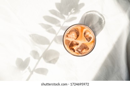 Cup of ice coffee with milk in white bed. Cold brew coffee. Flatlay, top view. Minimalism. Morning with sunlight.