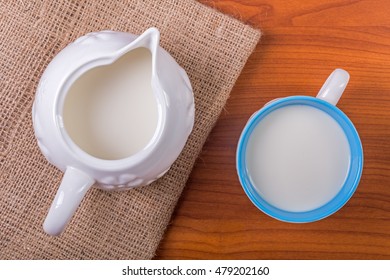 Cup And Jug Of Milk On Juta And Wooden Table - Top View