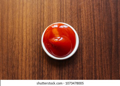 A Cup Of Ketchup Place On Wooden Table.