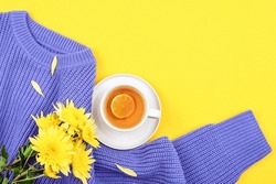 A Cup Of Lemon Tea, Yellow Chrysanthemum Flowers On Purple Knitted Sweater On Yellow Background. Top View, Flat Lay, Copy Space