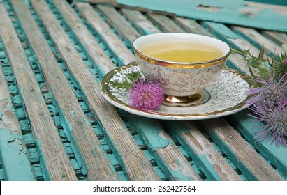 A Cup Of Milk Thistle Tea. Milk Thistle Blossoms Are In The Background