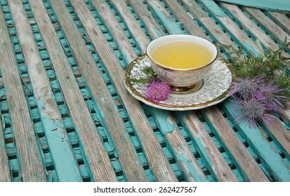 A Cup Of Milk Thistle Tea. Milk Thistle Blossoms Are In The Background