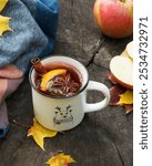 Cup with mulled wine, spices, yellow maple leaves, scarf, plaid, apple on a wooden surface. Autumn drink in nature, in the park.