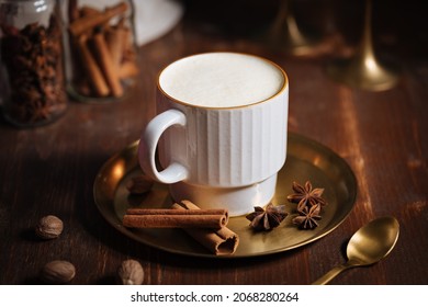Cup of pumpkin eggnog with golden spoon, cinnamon sticks, anise and nutmeg in a vintage atmosphere