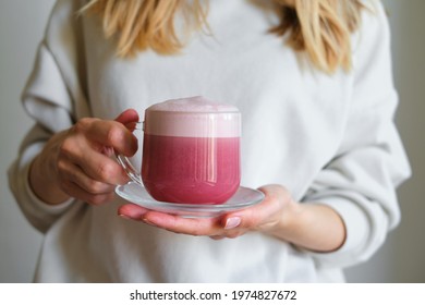 A cup of red velvet latte in the hands of a girl on a light background. Hot tasty drink. Trendy beetroot trendy drink with milk. A healthy alternative tasty dessert in a clear glass cup. Poster