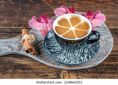 Cup of salep milky traditional hot drink of Turkey with cinnamon served in a porcelain cup beside pink orchid and cinnamon stick.