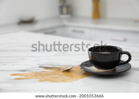 Cup and spilled coffee on white marble table in kitchen, space for text