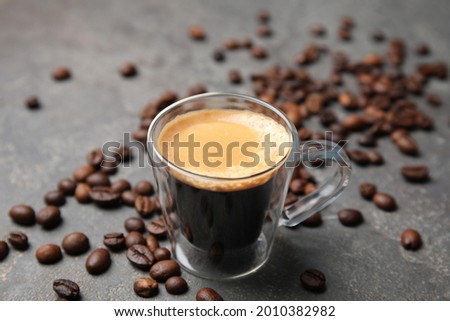 Cup of tasty espresso and scattered coffee beans on grey table