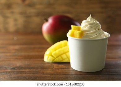 Cup of tasty frozen yogurt with mango on wooden table. Space for text