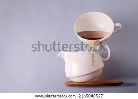 a cup of tea balances on a white ceramic teapot, copy space
