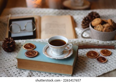 Cup of tea, books, tablet, bowl of cookies, various spices, pine cones and lit candles. Hygge at home. Selective focus. - Powered by Shutterstock