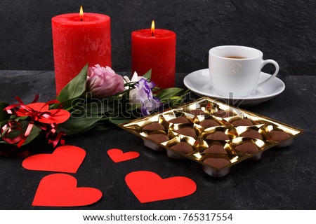 A cup of tea with a box of chocolates and candles on a stone background