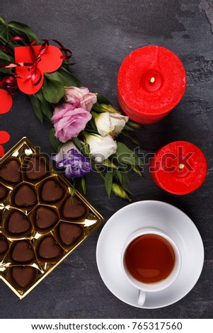 A cup of tea with a box of sweets showing not completely on a stone background