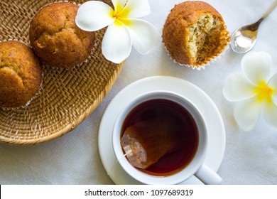 A Cup Of Tea And Cup Cakes Put On White Fabric Decorate With Frangipani Flowers, Top Down View.