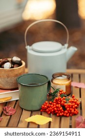 a cup of tea or coffee and a book on a wooden table against the background of fallen leaves, autumn season, still life with leaves, a book and viburnum and chestnuts in the garden outdoors. 