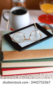 Cup of tea or coffee, stack of books, e-reader, glasses, various cookies, almonds, orange juice and lit candles on the table. Hygge at home. Selective focus.