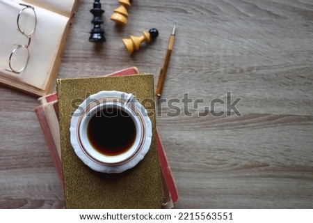 Cup of tea or coffee, stack of old books, reading glasses, pen and chess pieces on wooden table. dark academia concept. Top view.
