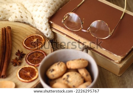 Cup of tea or coffee, various spices, bowl of cookies, tangerines, books, reading glasses and knitted blanket on wooden table. Hygge at home concept, selective focus.