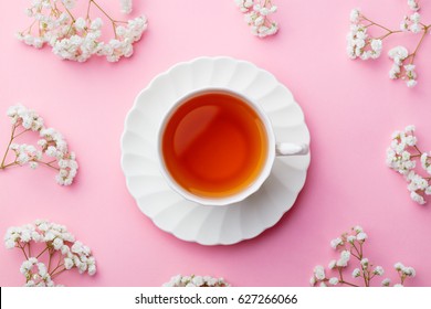 Cup of tea with fresh flowers on pink background. Top view. Copy space.
