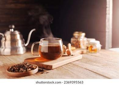Cup or tea glass Hot brew and dried tea leaves on a wooden plate, placed on a wooden table, on a dark black background.