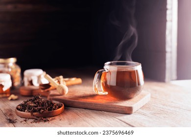 Cup or tea glass Hot brew and dried tea leaves on a wooden plate, placed on a wooden table, on a dark black background. - Powered by Shutterstock