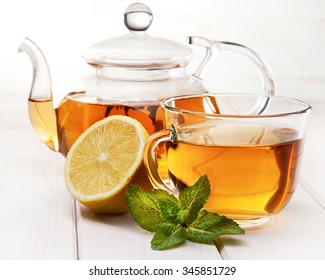 cup of tea, glass teapot, mint and lemon on a wooden table