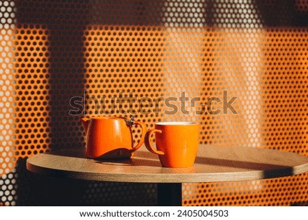 A cup of tea and a kettle in a minimalist orange cafe interior. Cozy cafe on a sunny morning. A warming drink in a minimalist interior, copy space.