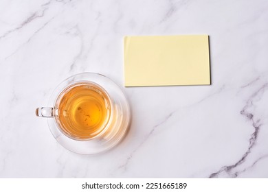 a cup of tea next to a blank note on a white marble table top view from above with copy space