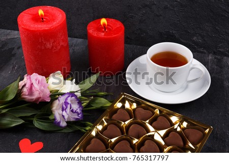 A cup of tea next to a box of chocolates and a bouquet of roses on a stone background