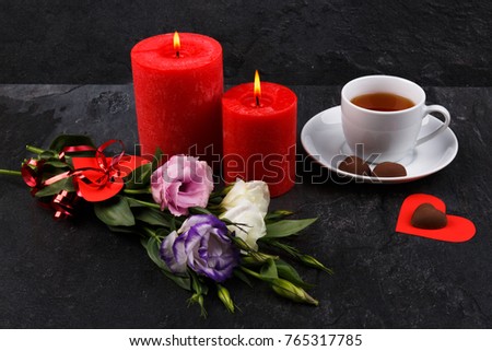 A cup of tea next to a candy on a heart, a bouquet of roses and burning roses on a stone background